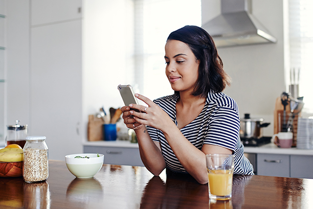 woman sits at the kitchen counter looking at her phone
