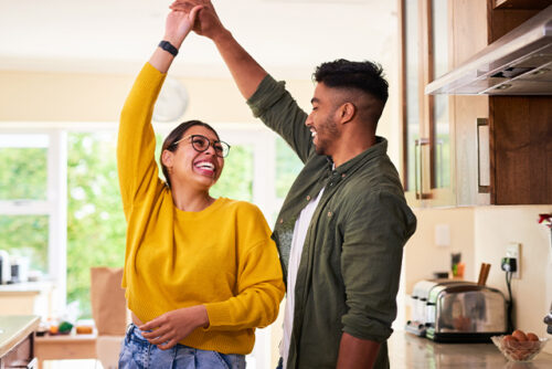Couple dances in the kitchen, smiling at each other