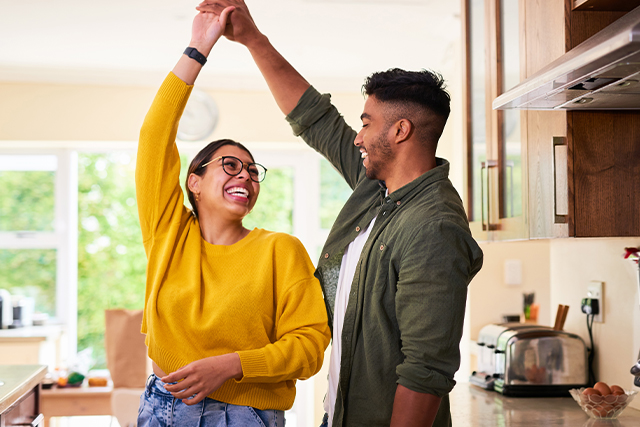 Couple dances in the kitchen, smiling at each other