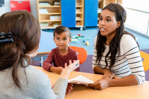 Parent and child sit at table with teacher