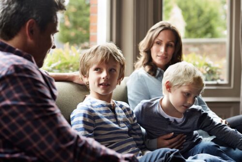 Parent with two children sit on the couch with their parents