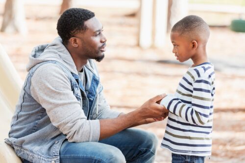 Father kneels down and holds his son's hands