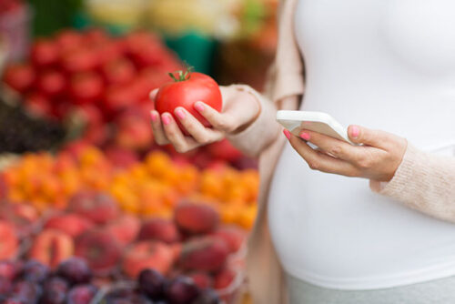pregnant woman holding tomato and smartphone