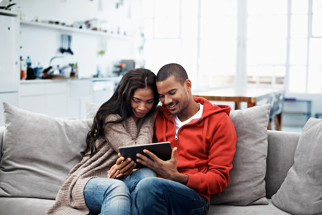 A couple sitting on the couch and looking at their tablet.