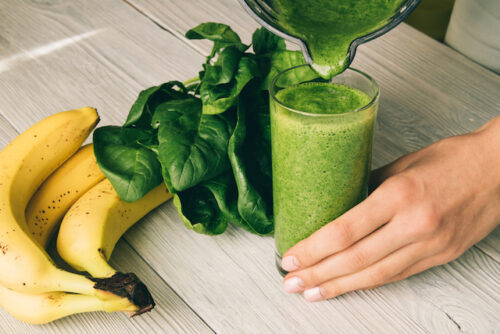 A person putting bananas and spinach into their smoothie.