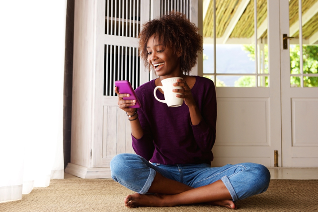 A person laughing while on their phone and drinking out of a mug.