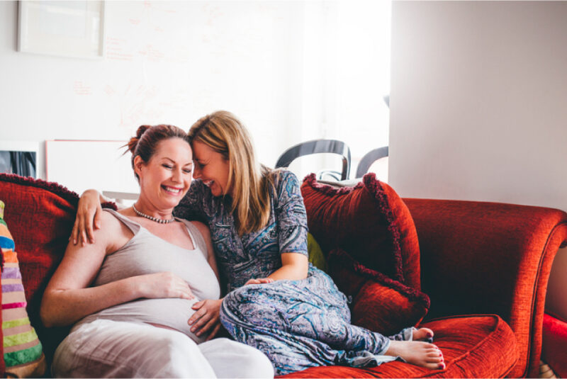 Pregnant woman and her wife cuddling on couch