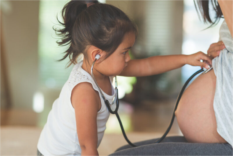 Toddler using stethoscope on her mom's pregnant belly