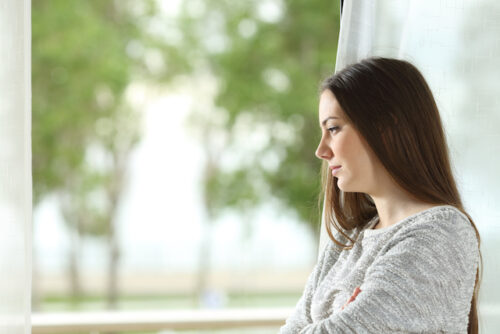 A person looking out the window with a sad expression.