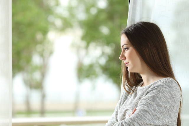 A person looking out the window with a sad expression.