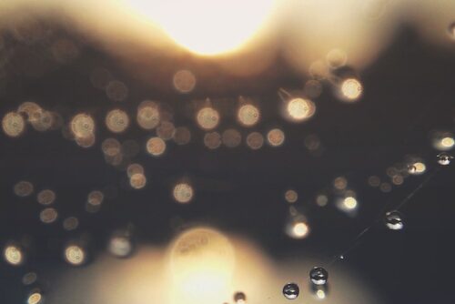 Image of light shining through a glass window that has water droplets on it.