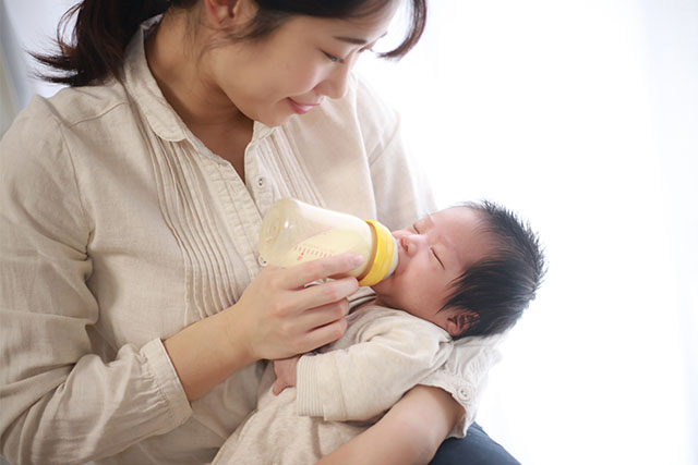 A woman holds her newborn baby and feeds them a bottle.