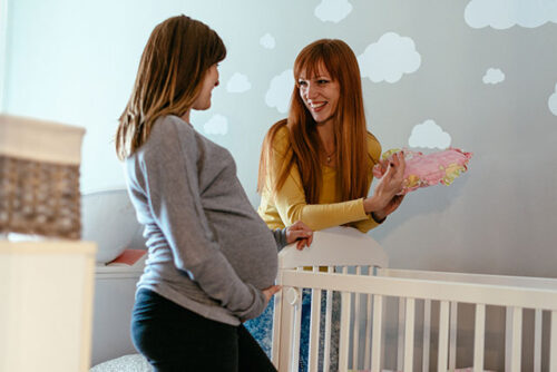 pregnant woman and friend stand over crib