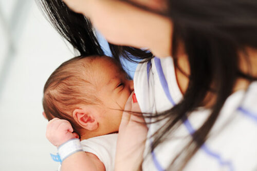 A woman breastfeeding newborn to represent how to get a newborn to latch on.