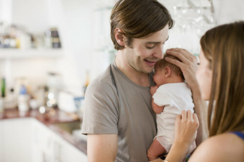 One person teaching another how to hold a newborn baby.