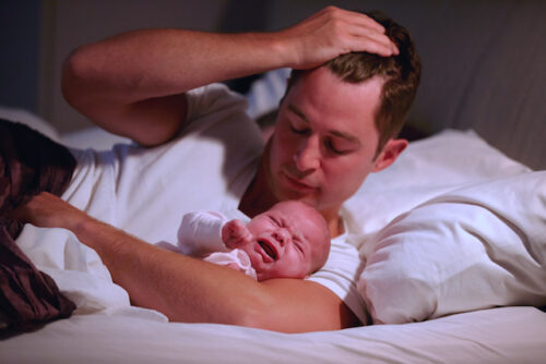 A person holding their crying baby wondering how to get the baby to sleep through the night.