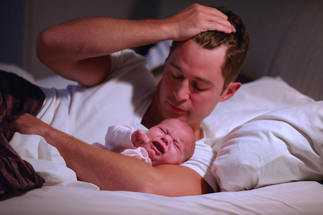 A person holding their crying baby wondering how to get the baby to sleep through the night.