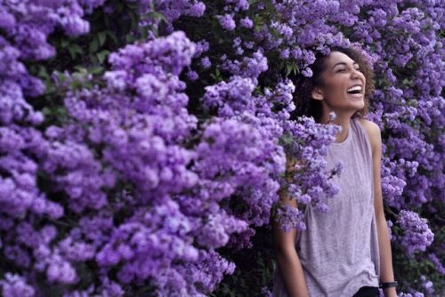 A person laughing next to some purple flowers.