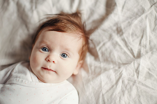 A newborn baby laying on bed to represent newborn hearing development.
