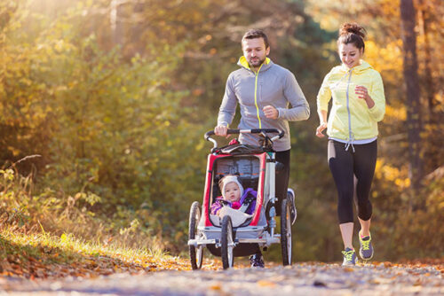 A couple running with baby to represent exercise while breast feeding.