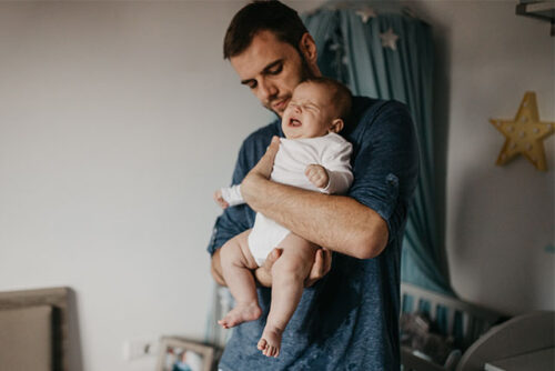 A dad soothing a crying newborn to represent what to do for a baby with colic.