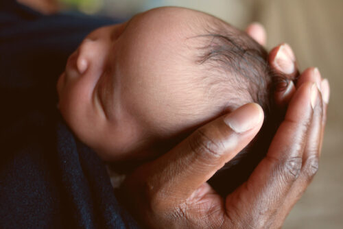 A person holding their newborn baby's soft spot.