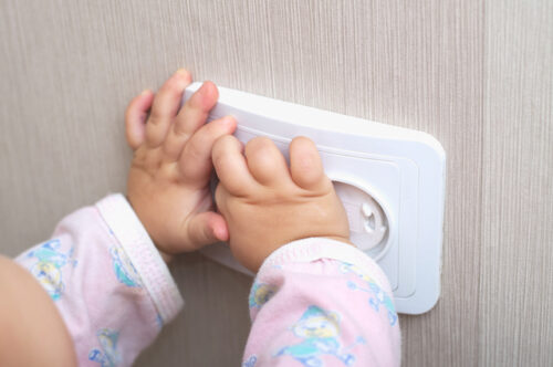 Two baby hands touching an outlet that's made safe by a cover. This is to represent baby proofing your house.