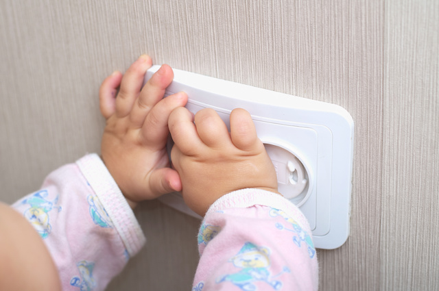 Two baby hands touching an outlet that's made safe by a cover. This is to represent baby proofing your house.
