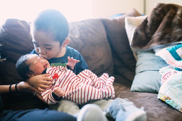 A little boy kissing newborn sibling.