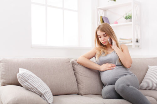A pregnant person sitting on the couch looking sad to represent a sign of depression.