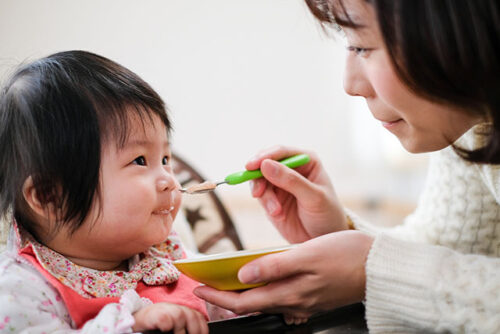 A person feeding prepared baby food in a jar.