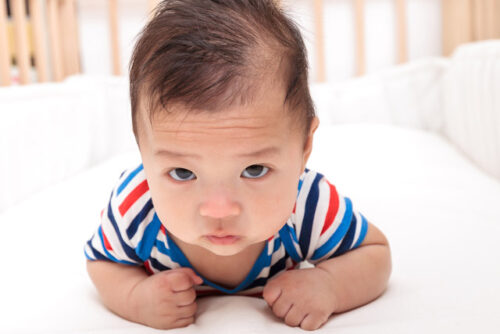 A baby laying on their stomach in a crib.