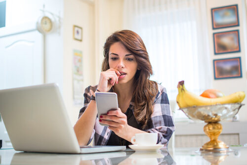 A person checking their phone while also using her laptop to research information about the BRCA gene.