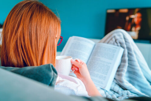 Woman in bed trying to increase her deep sleep by reading and drinking tea.