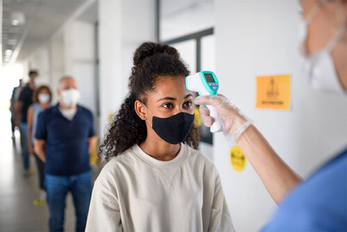 Woman gets her temperature taken while wondering if she should get the COVID 19 vaccine.