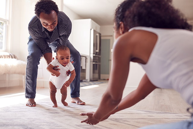 dad helping baby walk to mom