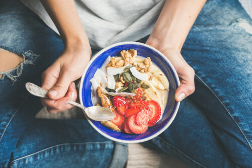 A person using a spoon to eat from a bowl of oats and strawberries to represent foods to eat while trying to conceive.
