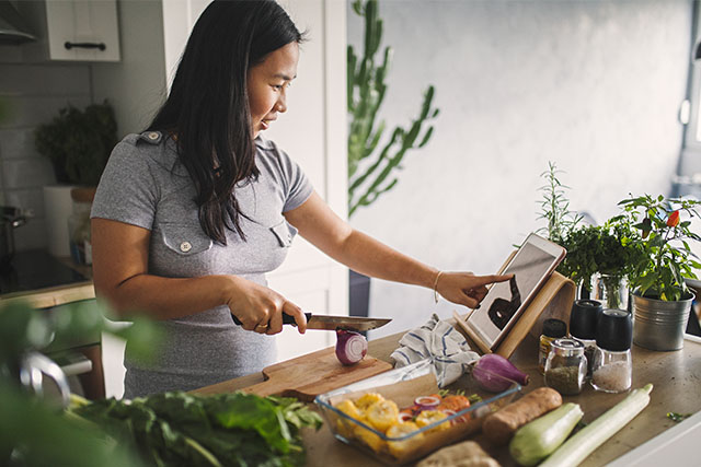 A woman cutting up vegetables in the kitchen to represent eating healthy to help fertility.