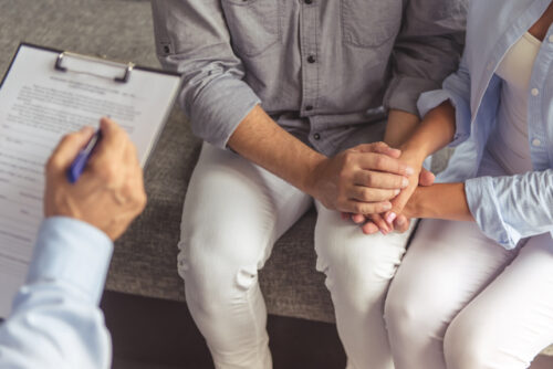 A couple talking to a medical professional with a clipboard about infertility testing.