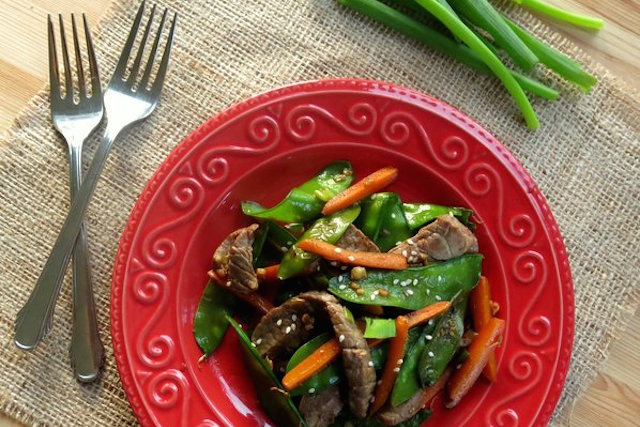 A red plate of sesame beef and stir fry.