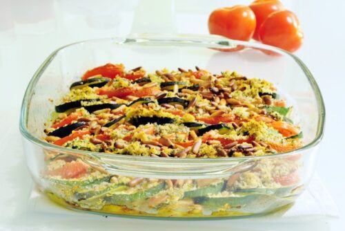 A dish of zucchini tomato tian with three full tomatoes sitting next to it.