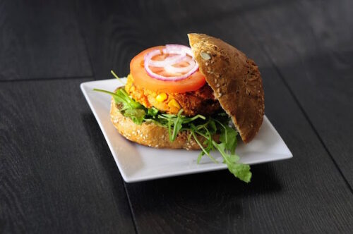 A sweet potato burger with a bun falling off the side of it on a white plate .