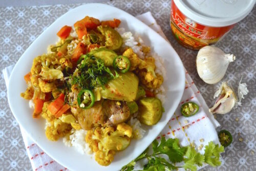 A plate of chicken red Thai curry next to a drink.