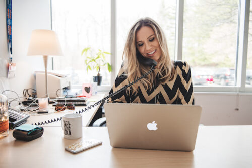 A person talking on the phone while using their laptop to represent stress when trying to conceive.