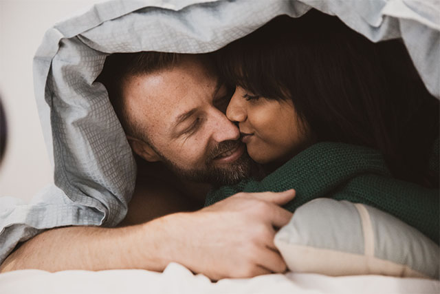 A couple in bed smiling and holding each other.