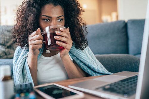 A woman drinking tea while looking up information on her computer about herbal remedies for fertility during ovulation.