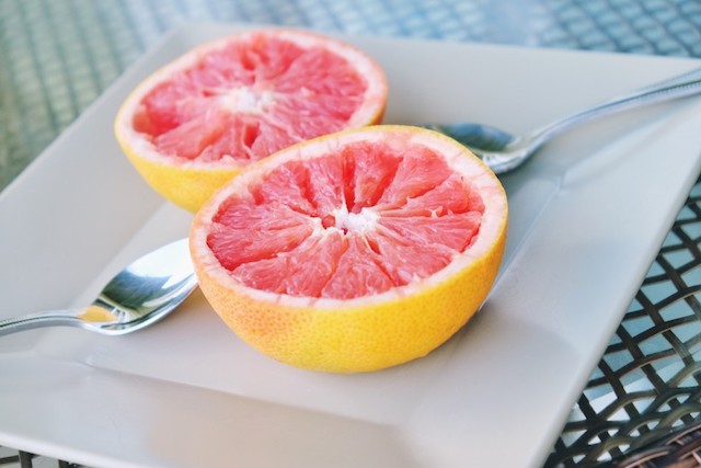 A grapefruit cut in half next to two spoons on a white plate.