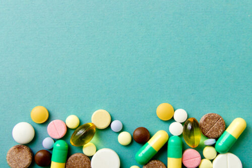 Pills and tablets on a teal background to represent prenatal vitamins.