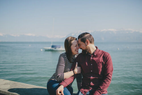 A couple looking into each others eyes while sitting by a body of water.