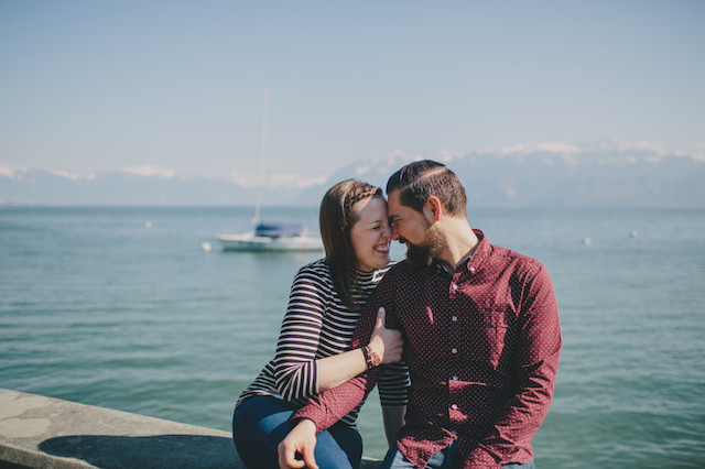A couple looking into each others eyes while sitting by a body of water.